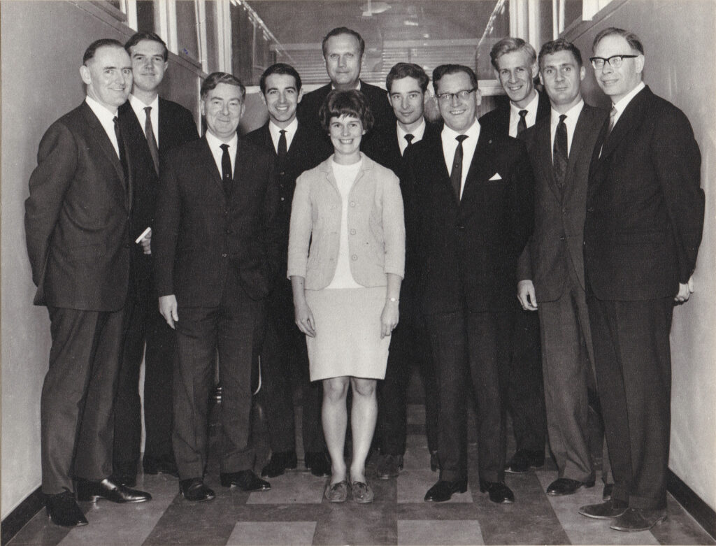 At center of photo, my mother. Around her, ten men. Location is IBM in London, 1966.